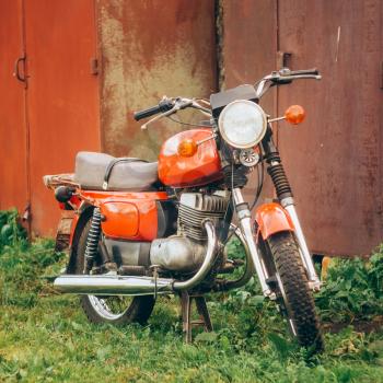 Old Red Motor Cycle Parked On Green Grass Yard. Vintage Generic Motorcycle Motorbike In Countryside