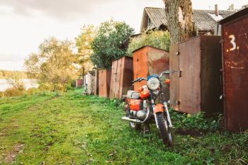 Old Red Motor Cycle Parked On Green Grass Yard. Vintage Generic Motorcycle Motorbike In Countryside