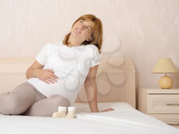 Happy pregnant girl lying on the bed on his stomach lie booties for newborn