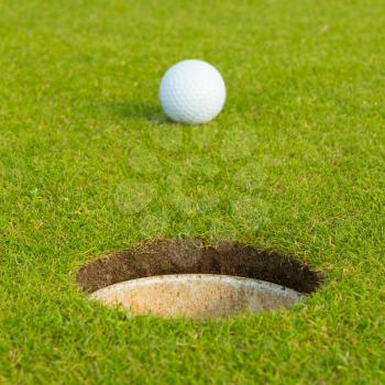 Golf ball on a green, in front of the hole, focus on the hole