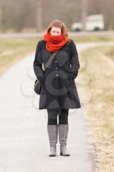 Woman dressed in warm clothing, standing on a small road