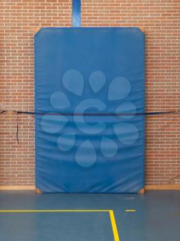 Large blue mat strapped to a brick wall, gym