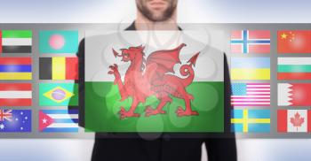 Hand pushing on a touch screen interface, choosing language or country, Wales