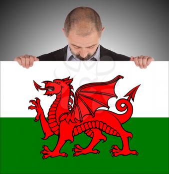 Businessman holding a big card, flag of Wales, isolated on white