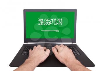 Hands working on laptop showing on the screen the flag of Saudi Arabia