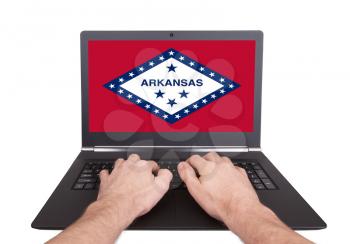 Hands working on laptop showing on the screen the flag of Arkansas