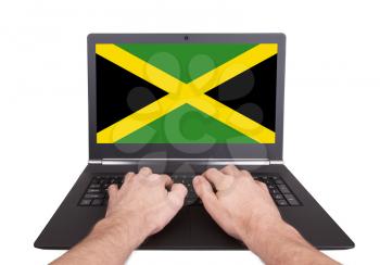 Hands working on laptop showing on the screen the flag of Jamaica