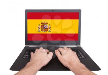Hands working on laptop showing on the screen the flag of Spain