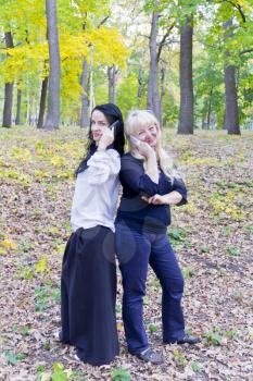 Two European women talking by mobile phone in autumn park