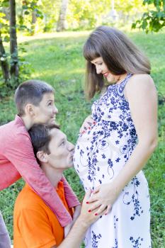 Happy family husband kissing pregnant wife stomach in summer time