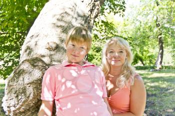 Blond woman and son in pink smiling under green crone of tree