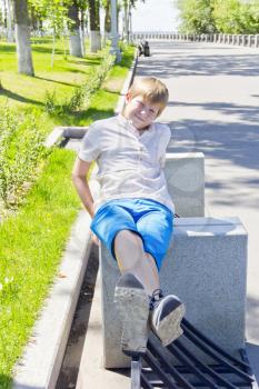 Blond boy sitting on concrete block in summer day