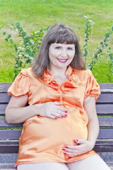 Pregnant woman with brown hair sitting in summer