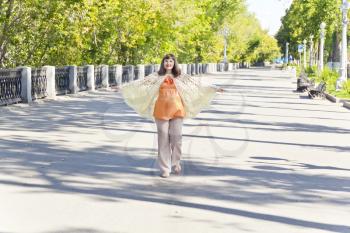 Pregnant woman with brown hair walking on embankment widely spaced arms