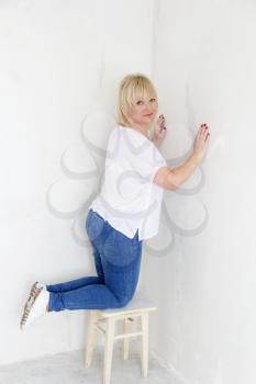Blond woman in white and blue jeans stand on her knee inside empty room
