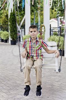 Cute brunette boy ride on a swing in summer