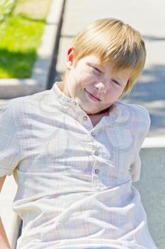 Blonde smiling boy sitting on a bench in summer park