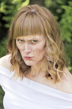 Vertical portrait of angry woman with blond hair on summer background