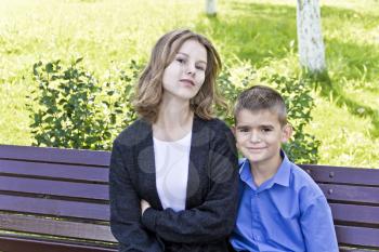 Brother and sister are sitting on bench in summer