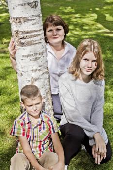 Happiest mother with daughter and son are sitting on green grass
