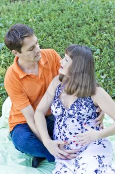Couple awaiting baby in orange on green grass