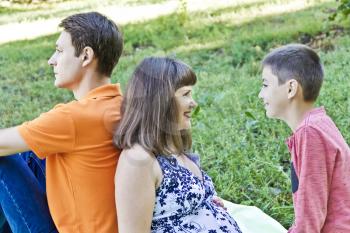 Happy family with pregnant mother are sitting on green grass