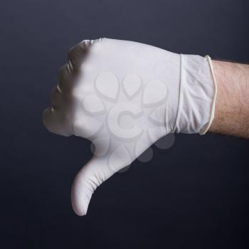 Male hand in latex glove (thumb down sign) on dark background