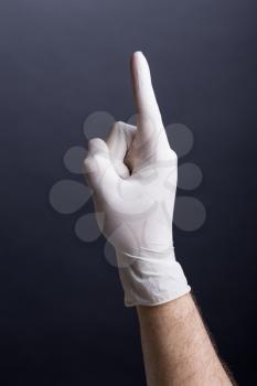 Male hand in latex glove (finger up) on dark background