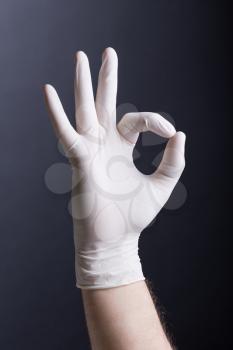 Male hand in latex glove (OK sign) on dark background
