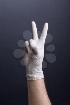 Male hand in latex glove (victory gesture, v-sign) on dark background