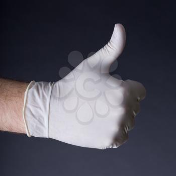 Male hand in latex glove. Thumb up sign. Great outcome, success, we will make it concept. Dark background