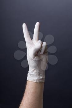 Male hand in latex glove. Doctor or nurse showing a victory sign. V-sign gesture on dark background. Success, we made it, it worked concept.