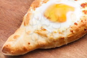 Ajarian khachapuri (Georgian cheese pastry), filled with cheese and topped with a soft-boiled egg and butter on wooden board close up
