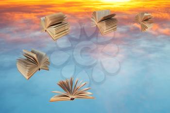 books fly over blue and yellow sunset clouds
