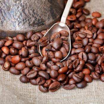 roasted coffee beans and copper coffee pot with spoon close up on textile