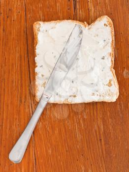 sandwich from toast and soft cheese with herbs, table knife on wooden table