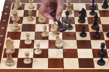 hand with black king knocks white king on chessboard in chess game