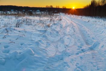 sunset under dark blue winter snowy country road