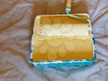painter roller brush in plastic paint tray with yellow emulsion paint