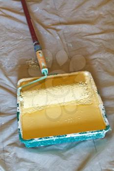 painter roller brush with handle in plastic paint tray with yellow emulsion paint