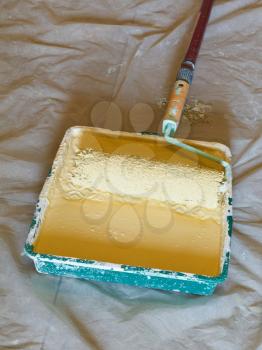 roller brush with handle in plastic paint tray with yellow emulsion paint
