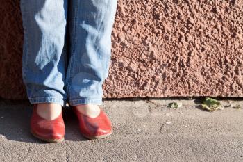 legs in blue jeans and red shoes near wall in autumn day