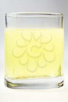 glass of yellow carbonated water on grey background