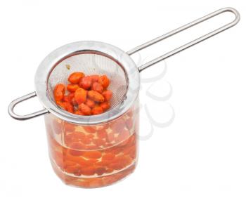 preparing of goji berry tincture - strainer and glass with goji berries infusion isolated on white background