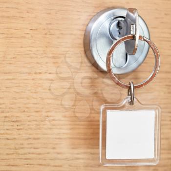 steel key with blank square keychain in lock of wooden door close up