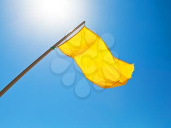warning yellow flag under sun with blue sky background