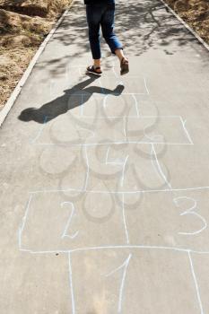 girl hops in hopscotch on urban alley in sunny day