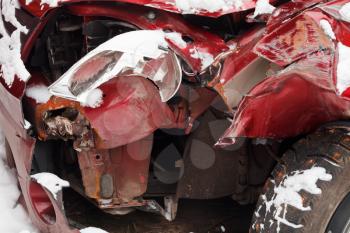 broken headlamp and crumpled hood of red car after winter traffic accident