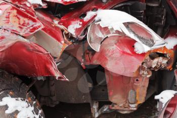 broken headlight and crumpled hood of red car after winter traffic accident