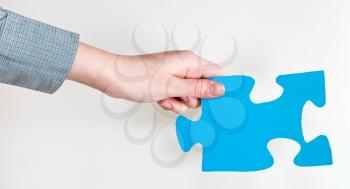 blue puzzle piece in female hand on grey background